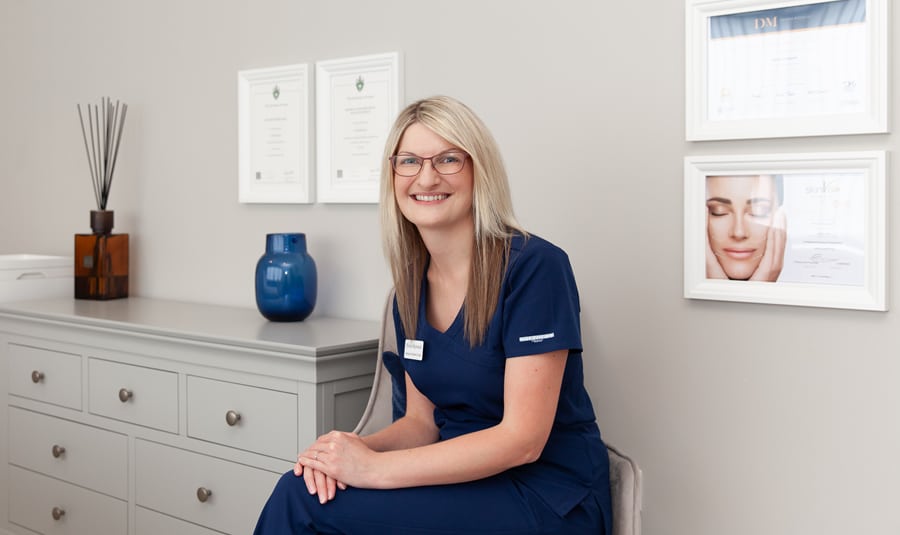 Nicola Haywood, aesthetic nurse in Wakefield, smiling in her clinic in front of her certificates and qualifications